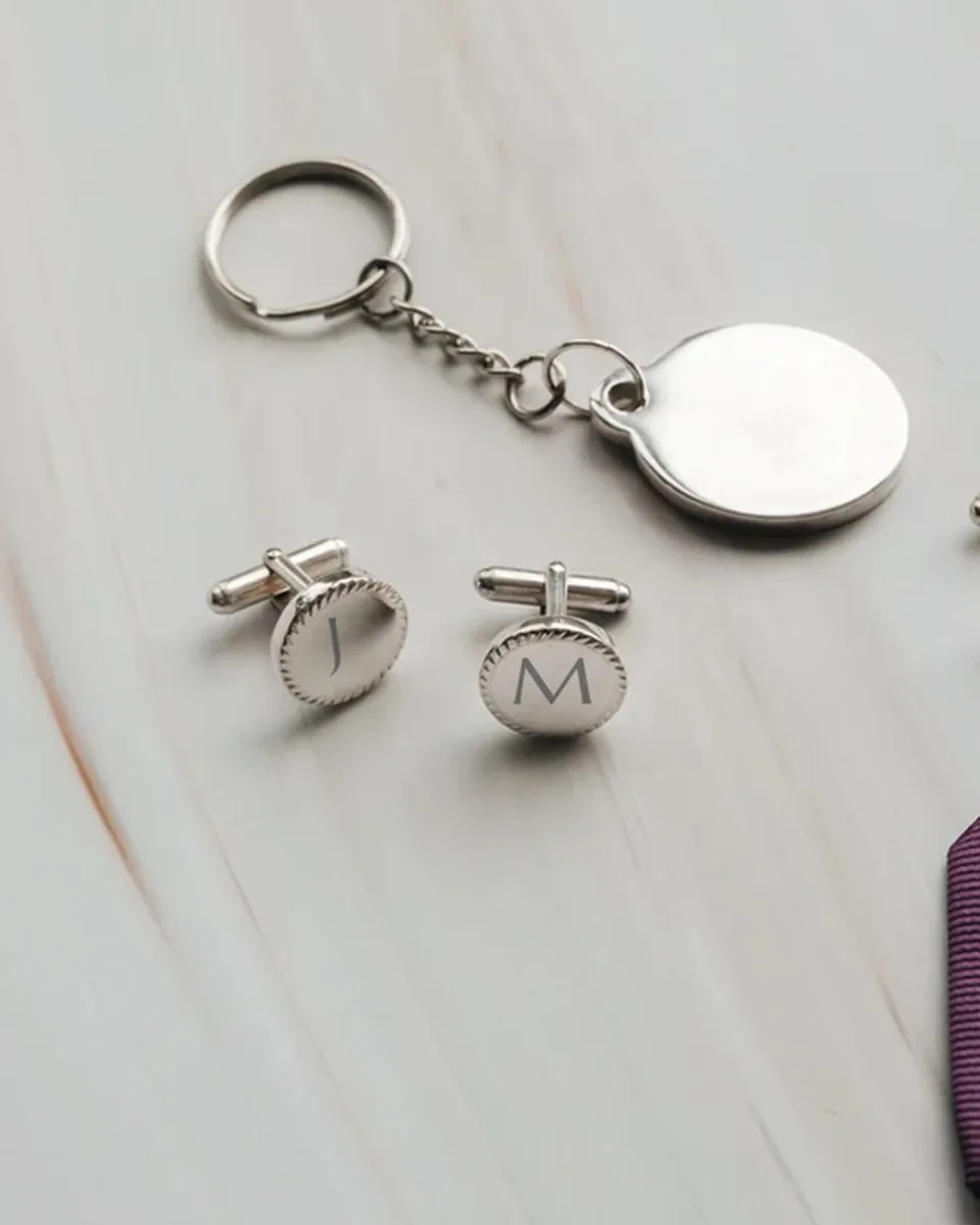 Boutons de manchette ronds en acier gravés J et M, avec un porte-clés et une pince à cravate, sur du marbre