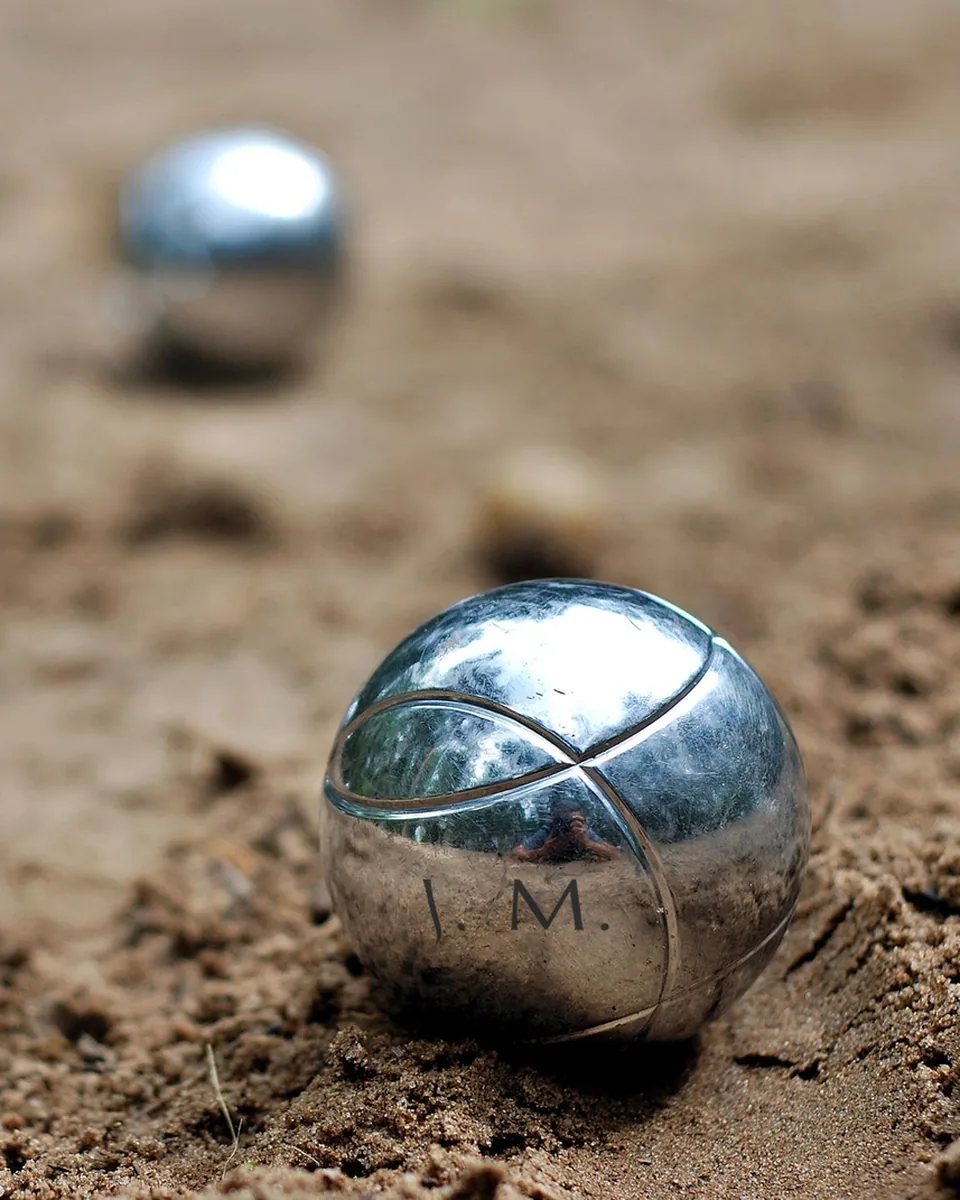 Boule de pétanque en acier gravée J. M., dans le sable