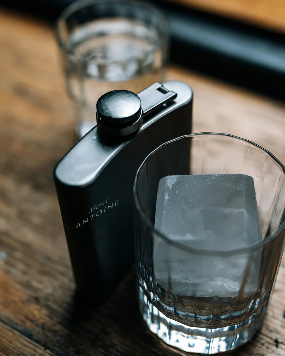 Flasque laquée noire gravée « Merci ANTOINE », à côté d'un verre de whisky