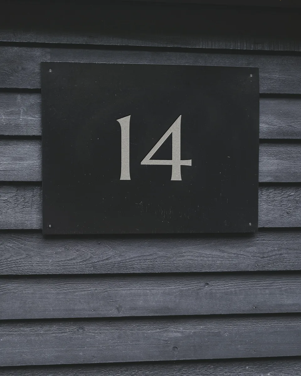 Plaque de numéro en ardoise gravée 14, vissée sur un bardage de bois gris