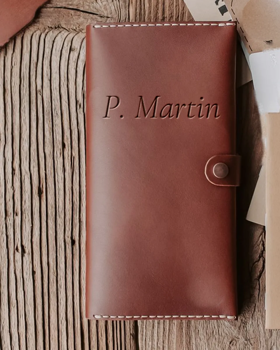 Étui long en cuir rouge-brun à pression, gravé « P. Martin », sur des planches de bois brut