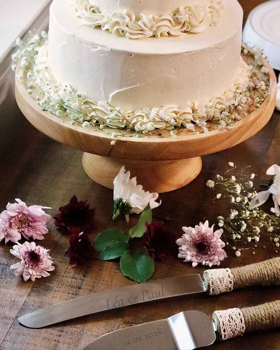 Couteau et pelle à gâteau devant un gâteau de mariage, lames gravées « Léa & Paul » et 14.06.2026