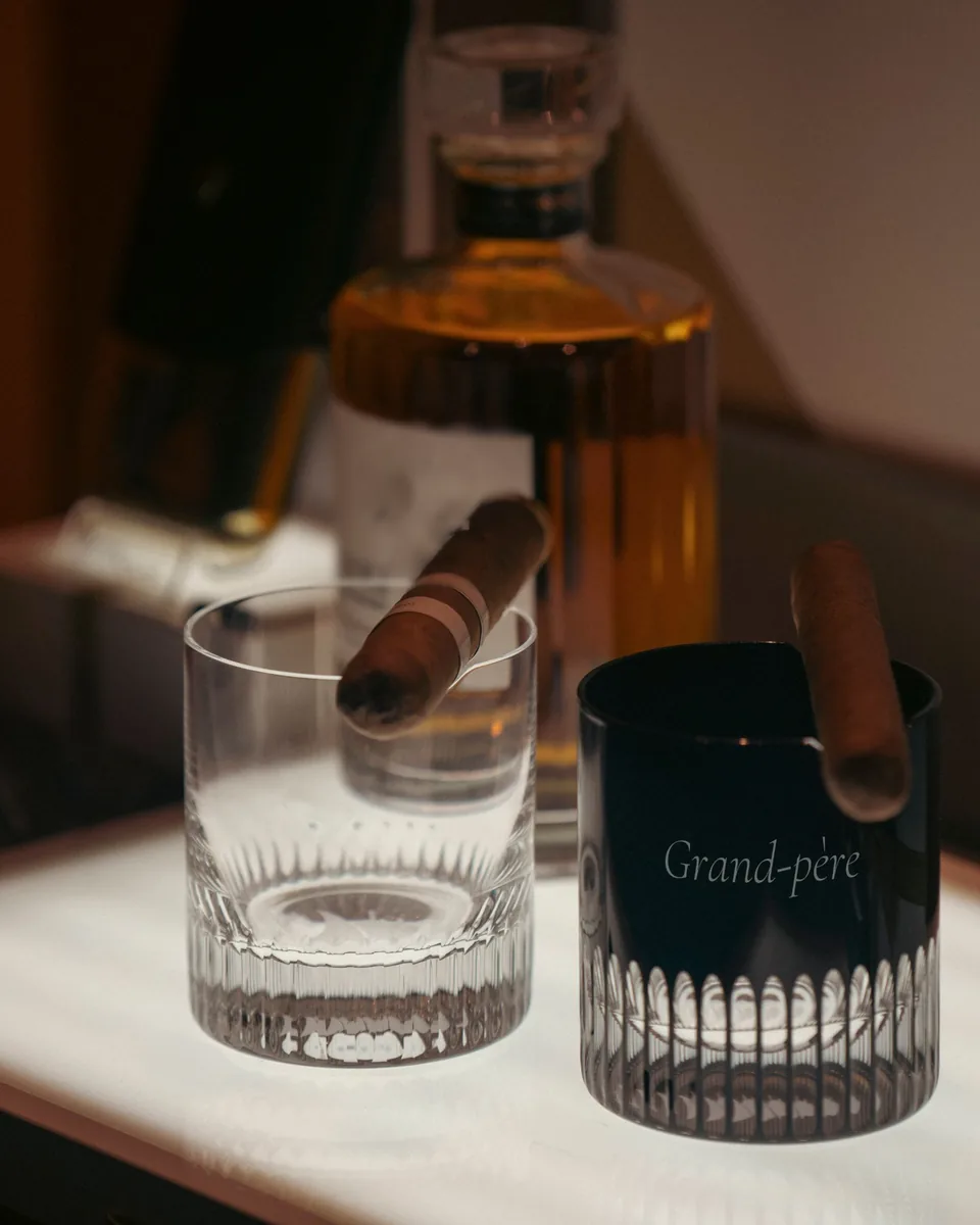 Deux verres à whisky à encoche, un cigare posé sur chacun, le verre fumé gravé « Grand-père »